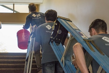 Workers wearing PSE ensignias climbing stairs carrying ladders and a bucket