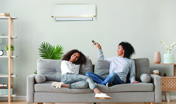 Mother points controller at wall mounted heat pump while sitting on sofa with daughter