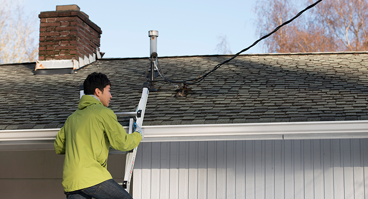 A man climbing onto his roof on a ladder