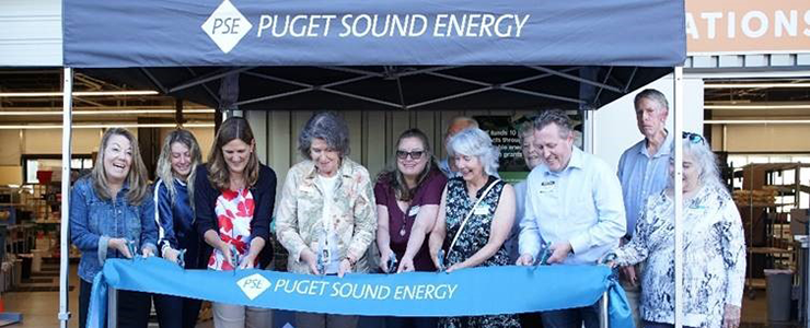 A group of nine people in ribbon cutting ceremony standing under a Puget Sound Energy banner