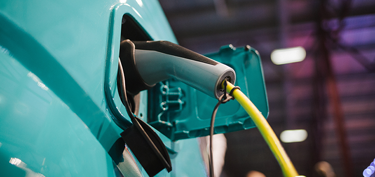 Reduce operations and maintenance costs by transitioning your fleet to electric vehicles with PSE Up & Go Electric for Fleet. A close-up view from the side of a greenish blue car, showing an EV charging nozzle plugged into its socket