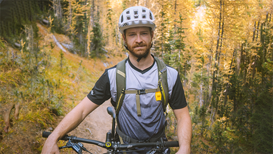 Hunter Hassig is shown wearing a bike helmet, standing with his bicycle, on a bike trail in the woods