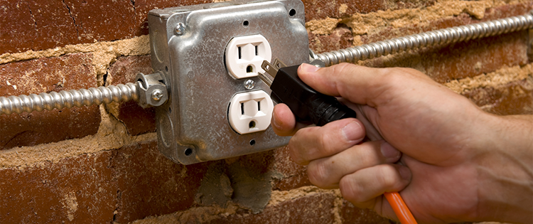 Một bàn tay cắm dây nguồn vào ổ cắm điện gắn trên tường gạch