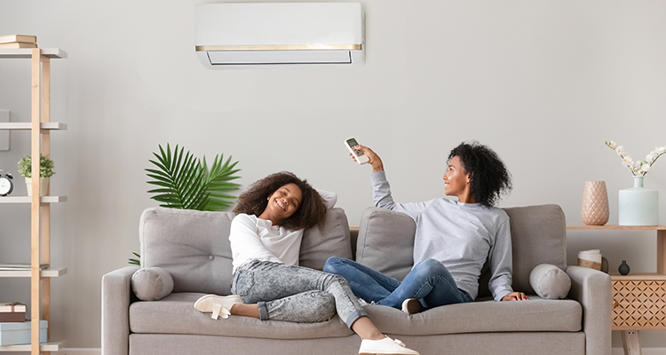 Smiling family members seated on couch, pointing remote control at home heating wall unit