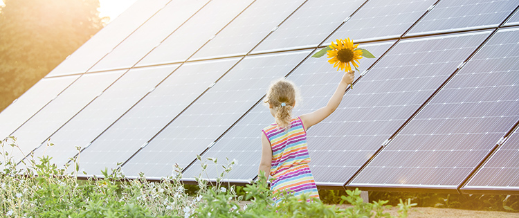 Una niña sosteniendo un girasol delante de un panel solar