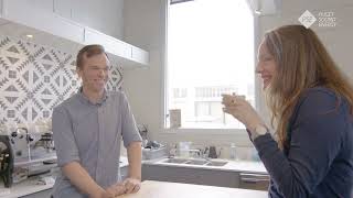 A  man and a woman in a kitchen, smiling with a cup of coffee